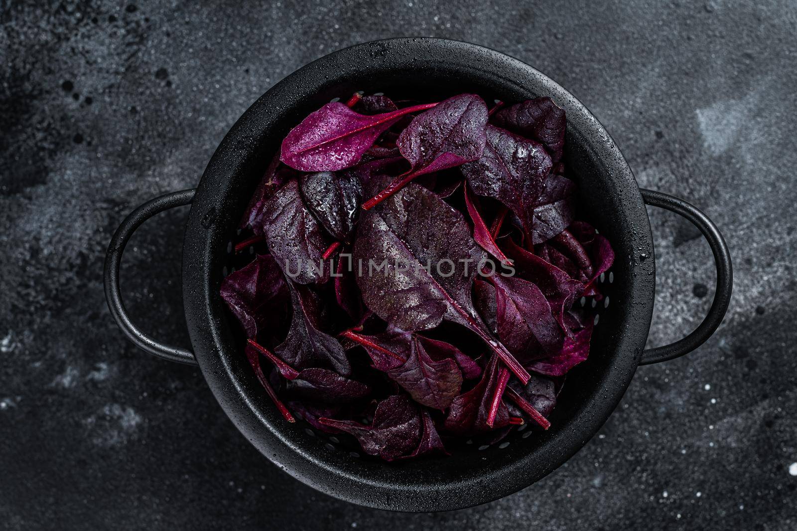 Leaves of Swiss red chard or Mangold salad in a colander. Black background. Top view by Composter