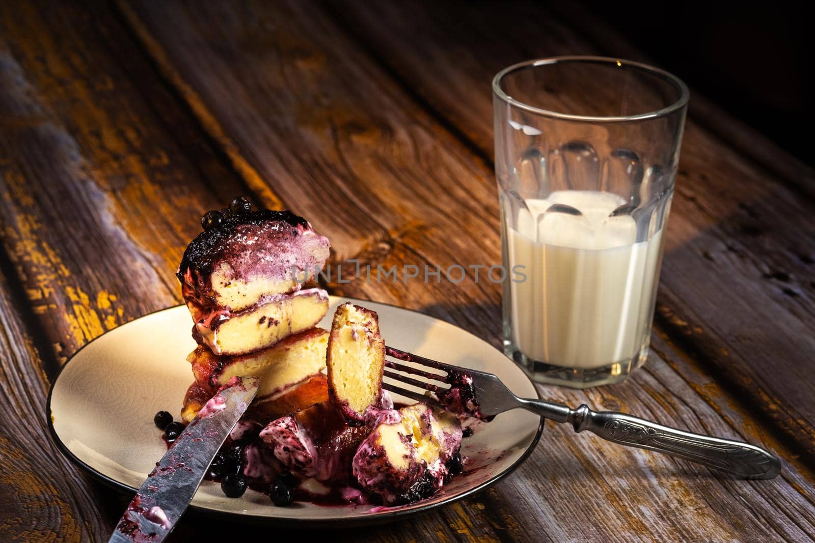 sliced cheesecakes with blueberry jam and sour cream on a plate and a glass of milk on a wooden table.