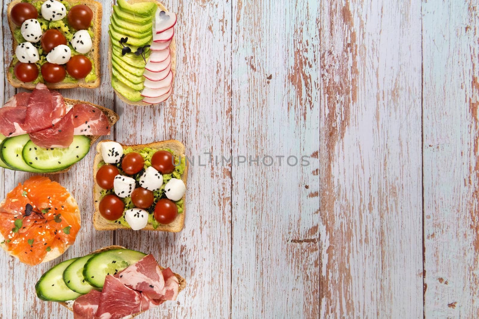 An assortment of sandwiches with fish, cheese, meat and vegetables lay on the wooden table by Lobachad