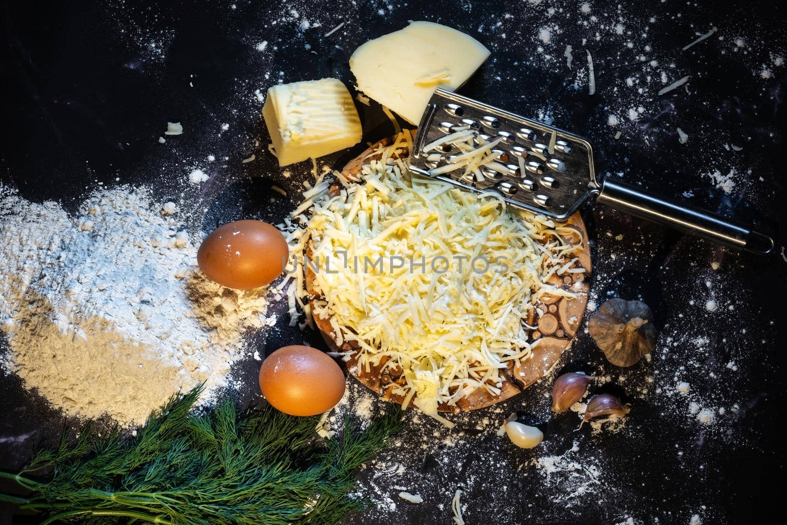Top view of a still life of the process of making cheese balls with garlic and dill on a black background.