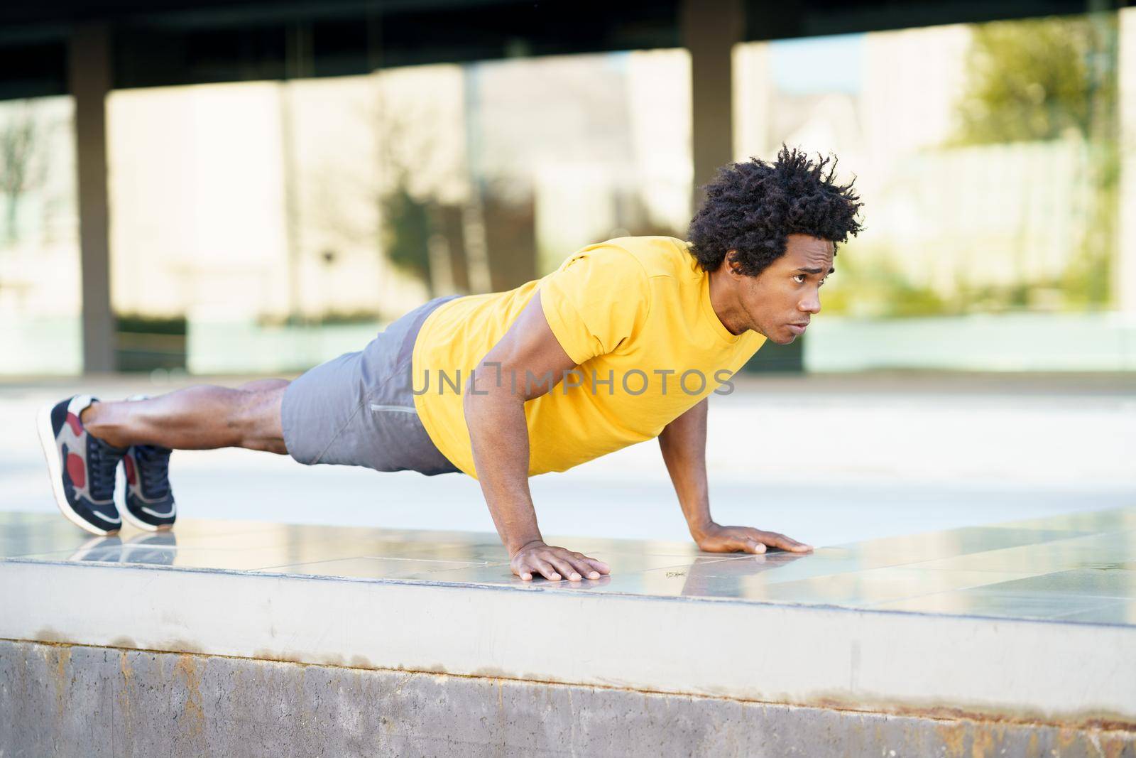 Black man doing triceps dip exercise on city street bench. by javiindy