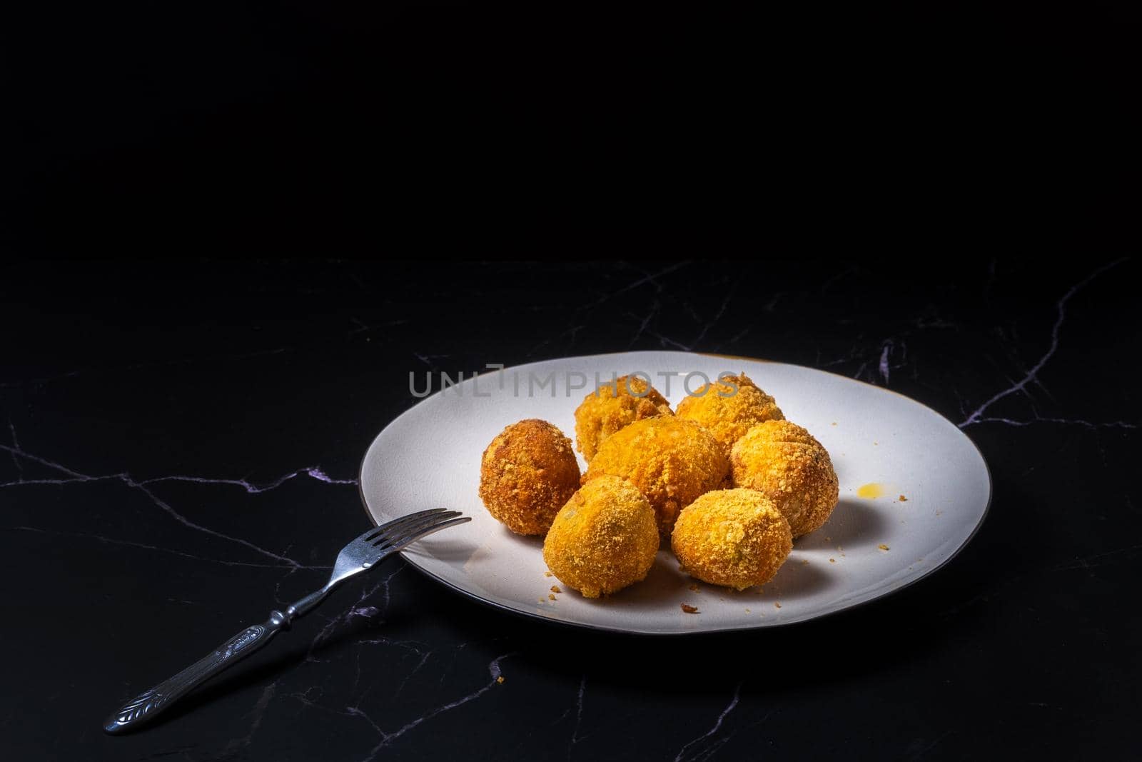 cheese balls with garlic and dill inside for a snack in a white plate on a black background.