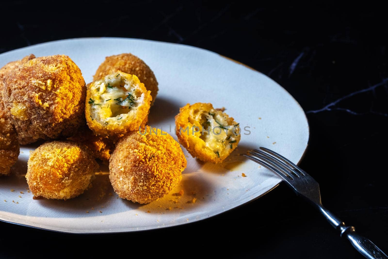 cheese balls with garlic and dill inside for a snack in a plate on a black background.