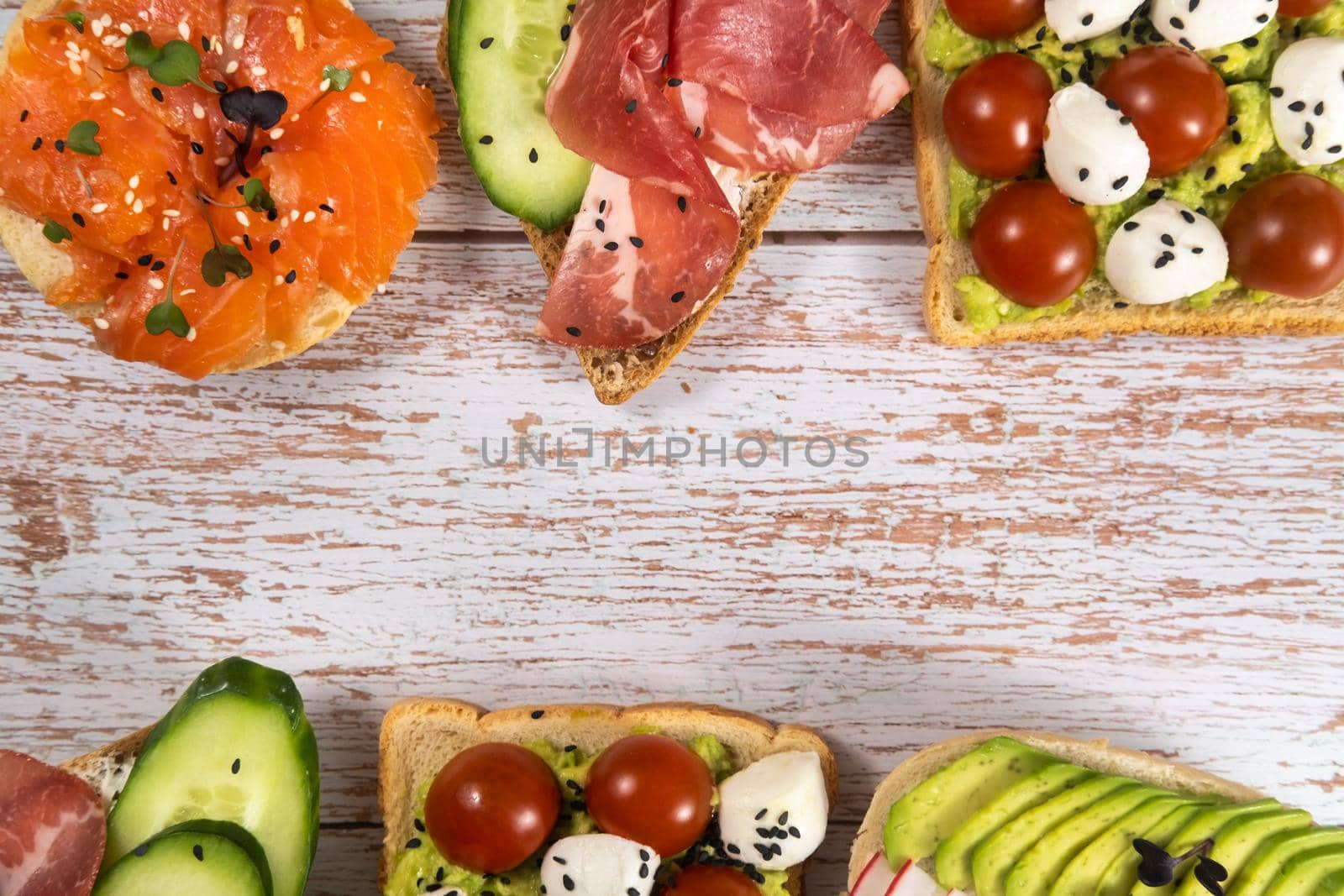 An assortment of sandwiches with fish, cheese, meat and vegetables lay on the wooden table.