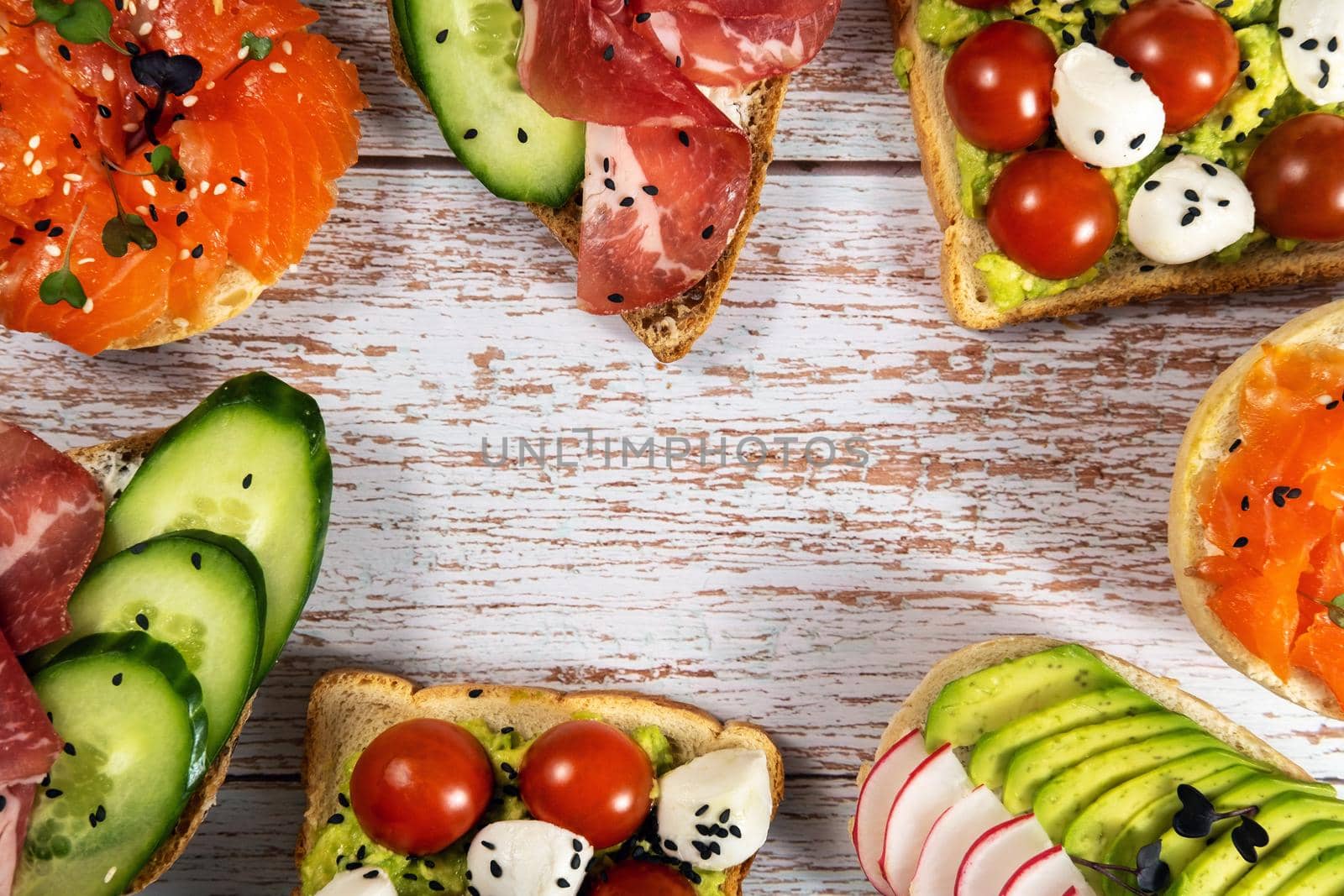 An assortment of sandwiches with fish, cheese, meat and vegetables lay on the wooden table by Lobachad