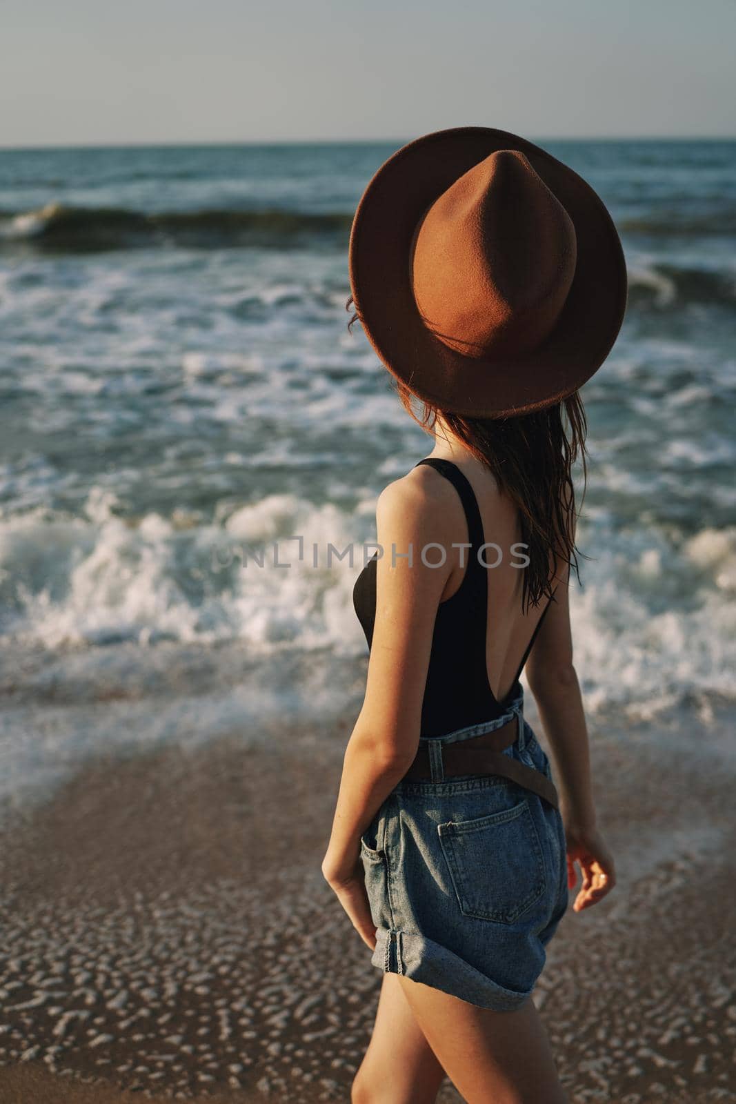 cheerful woman in sunglasses and a hat walks along the ocean. High quality photo