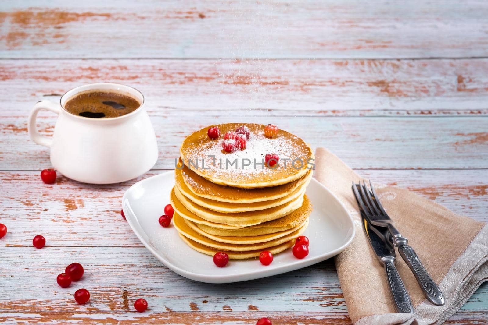 morning breakfast of pancakes with cranberries and powdered sugar and a cup of coffee on a wooden table.