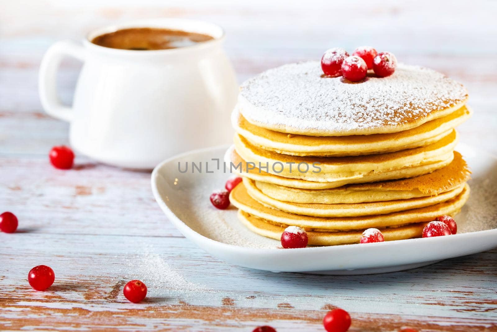 morning breakfast of pancakes with cranberries and powdered sugar on a wooden table and a cup of coffee.