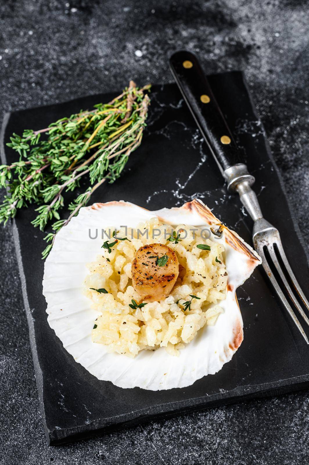 Risotto with pan seared sea scallops in a shell. Black background. Top view by Composter