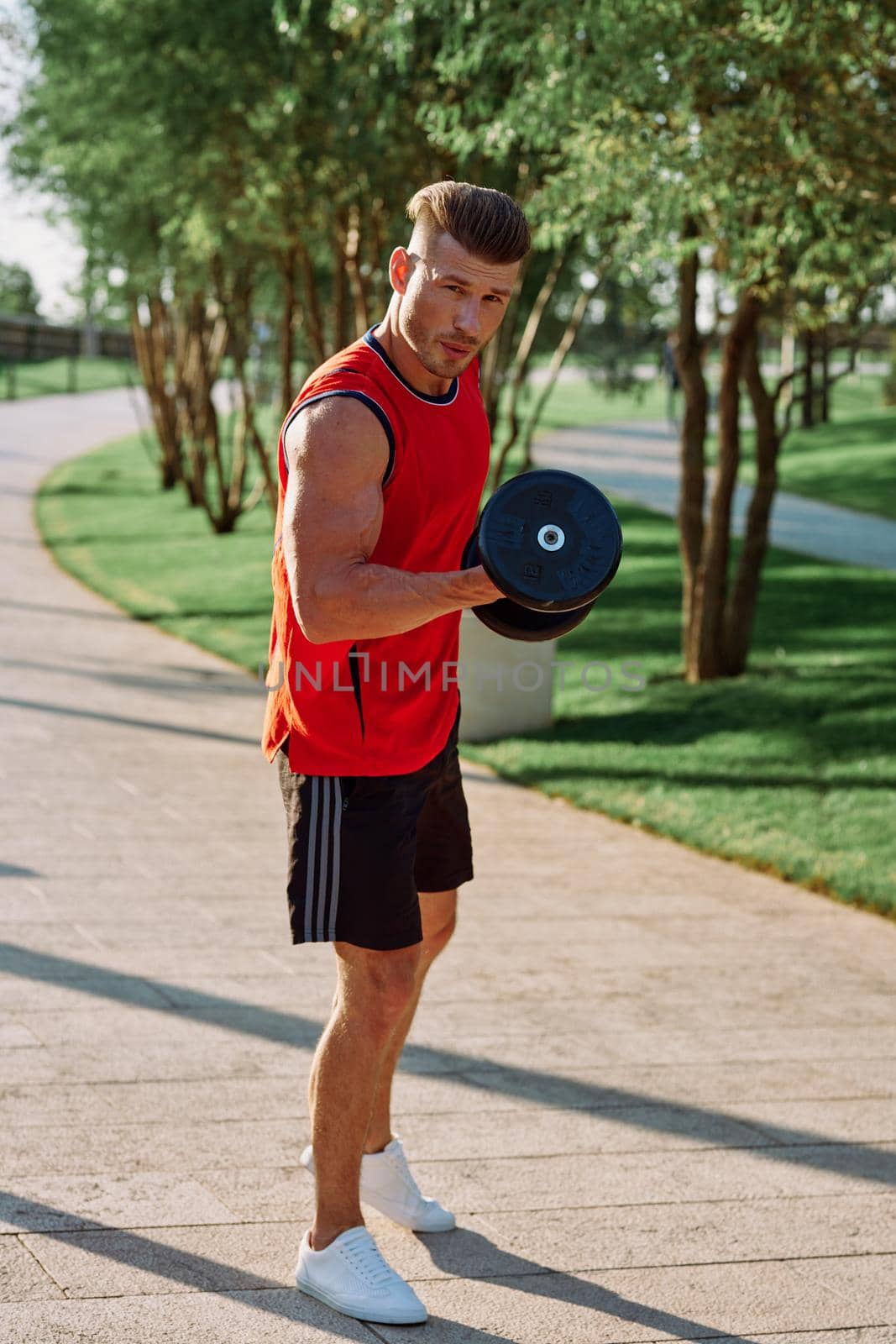 athletic man with dumbbells in his hands outdoors in the park by Vichizh