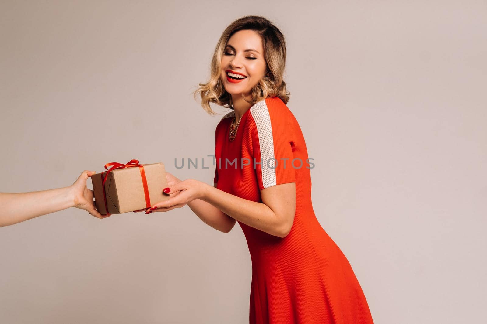 A girl in a red dress is given a gift in her hands on a gray background.