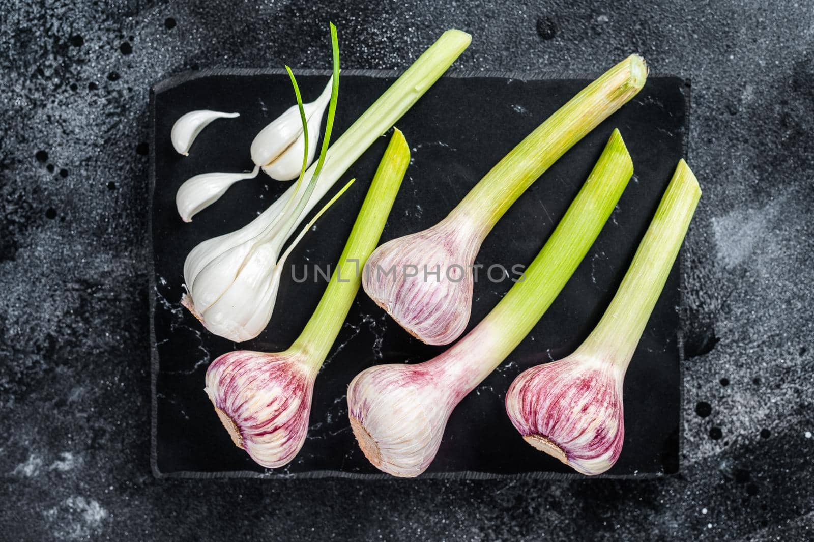 Raw Spring young garlic bulbs and cloves on marble board. Black background. Top view by Composter