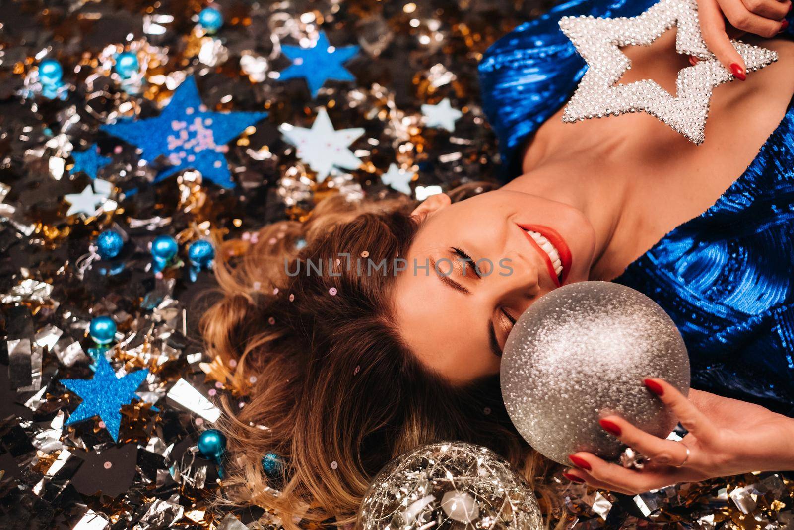 a woman in a blue sequined dress smiles and lies on the floor under a falling multicolored confetti by Lobachad