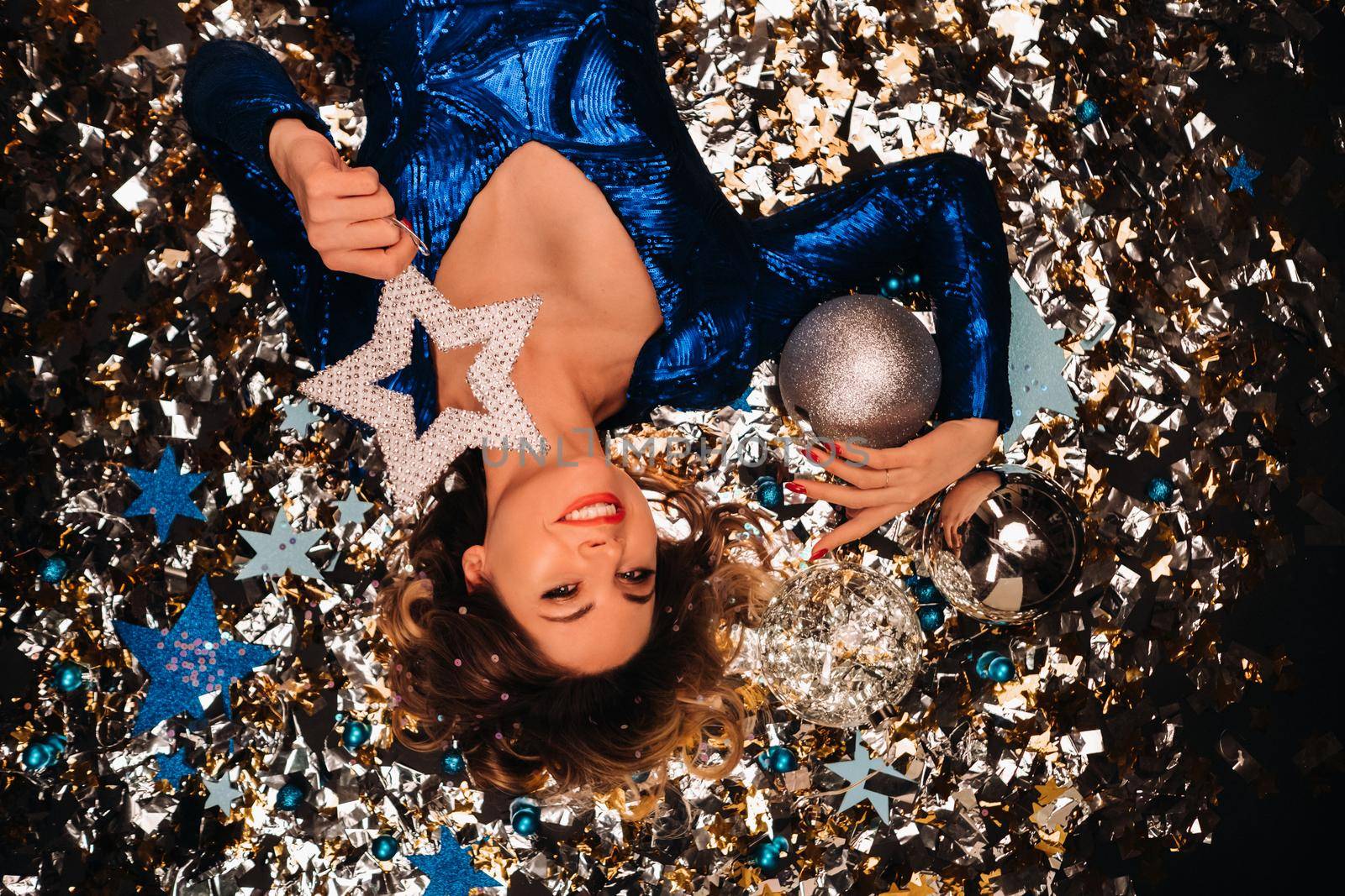 a woman in a blue sequined dress smiles and lies on the floor under a falling multicolored confetti by Lobachad