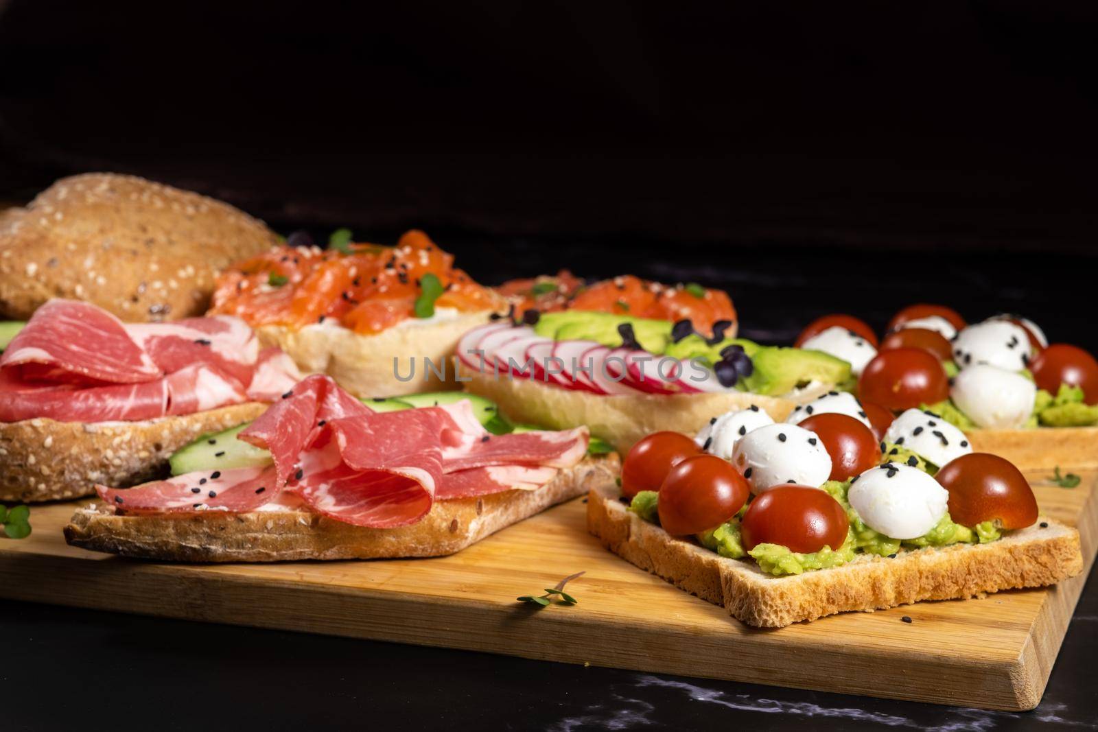 Assorted sandwiches with fish, cheese, meat and vegetables lying on the board.