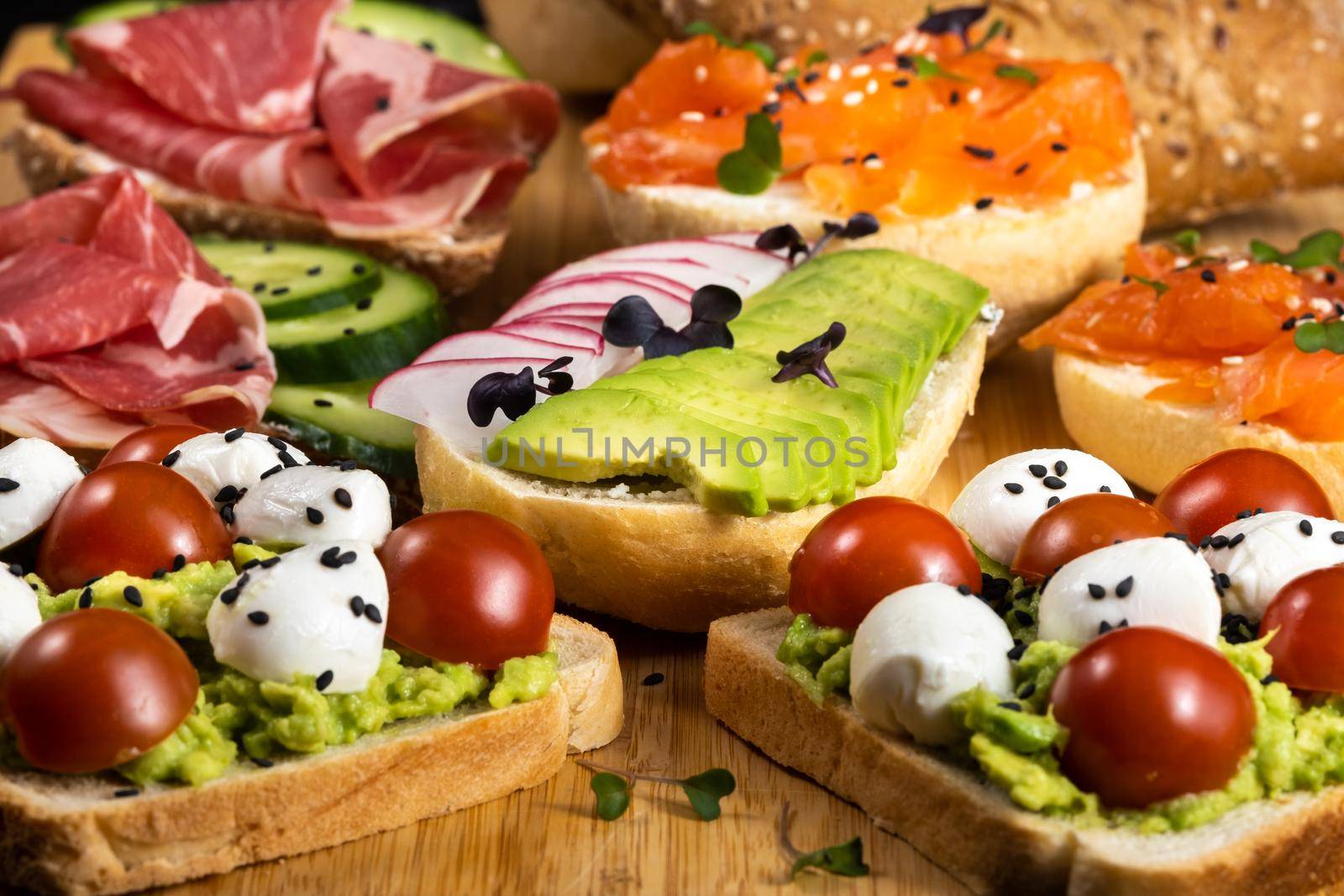 Assorted sandwiches with fish, cheese, meat and vegetables lying on the board.