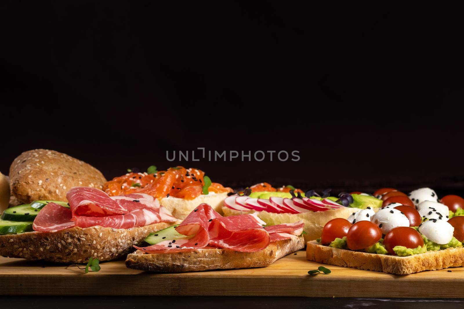 An assortment of sandwiches with fish, cheese, meat and vegetables lay on the board and a bun by Lobachad