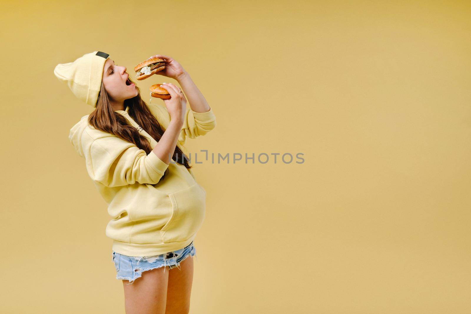 pregnant girl in yellow clothes with hamburgers in her hands on a yellow background by Lobachad