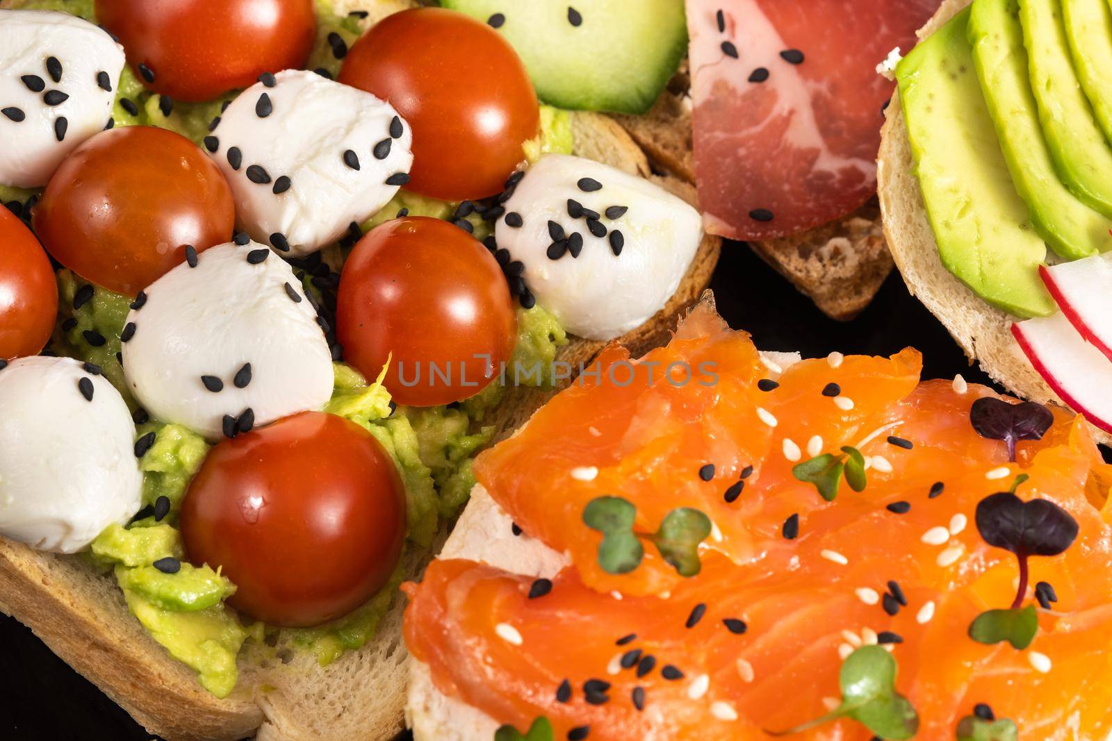 Assorted sandwiches with fish, cheese, meat and vegetables on a black plate.