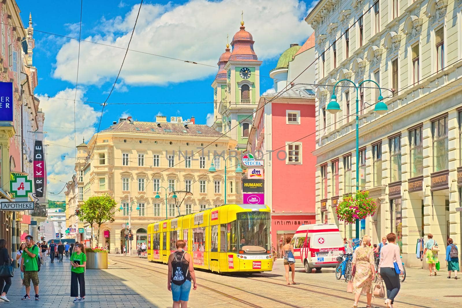 Linz - June 2020, Austria: view of the main street with walking people, yellow tram, and old colorful historical buildings