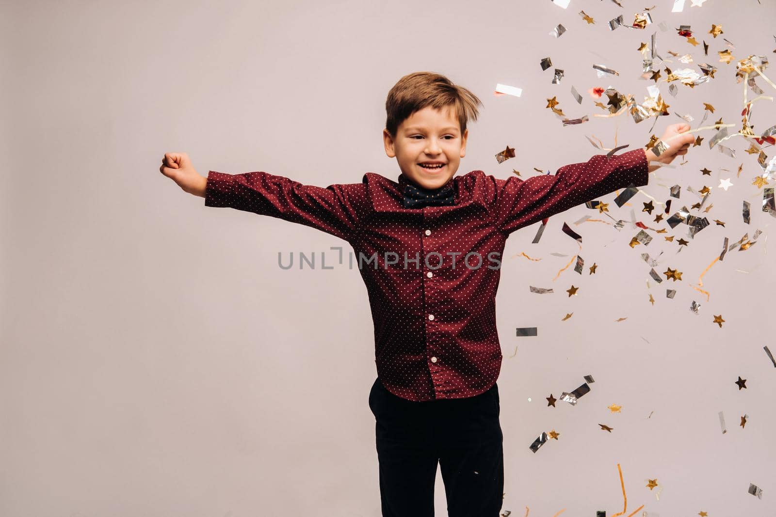 Beautiful boy jumping for joy and with confetti on a gray background.