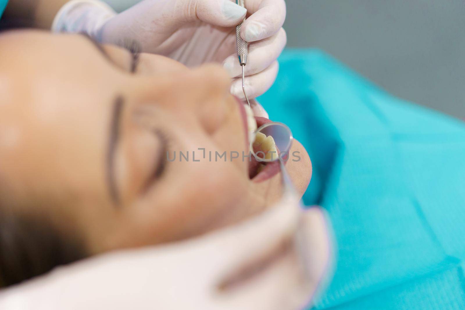 Dentist checking the inside of her female patient's teeth with a dental mirror.