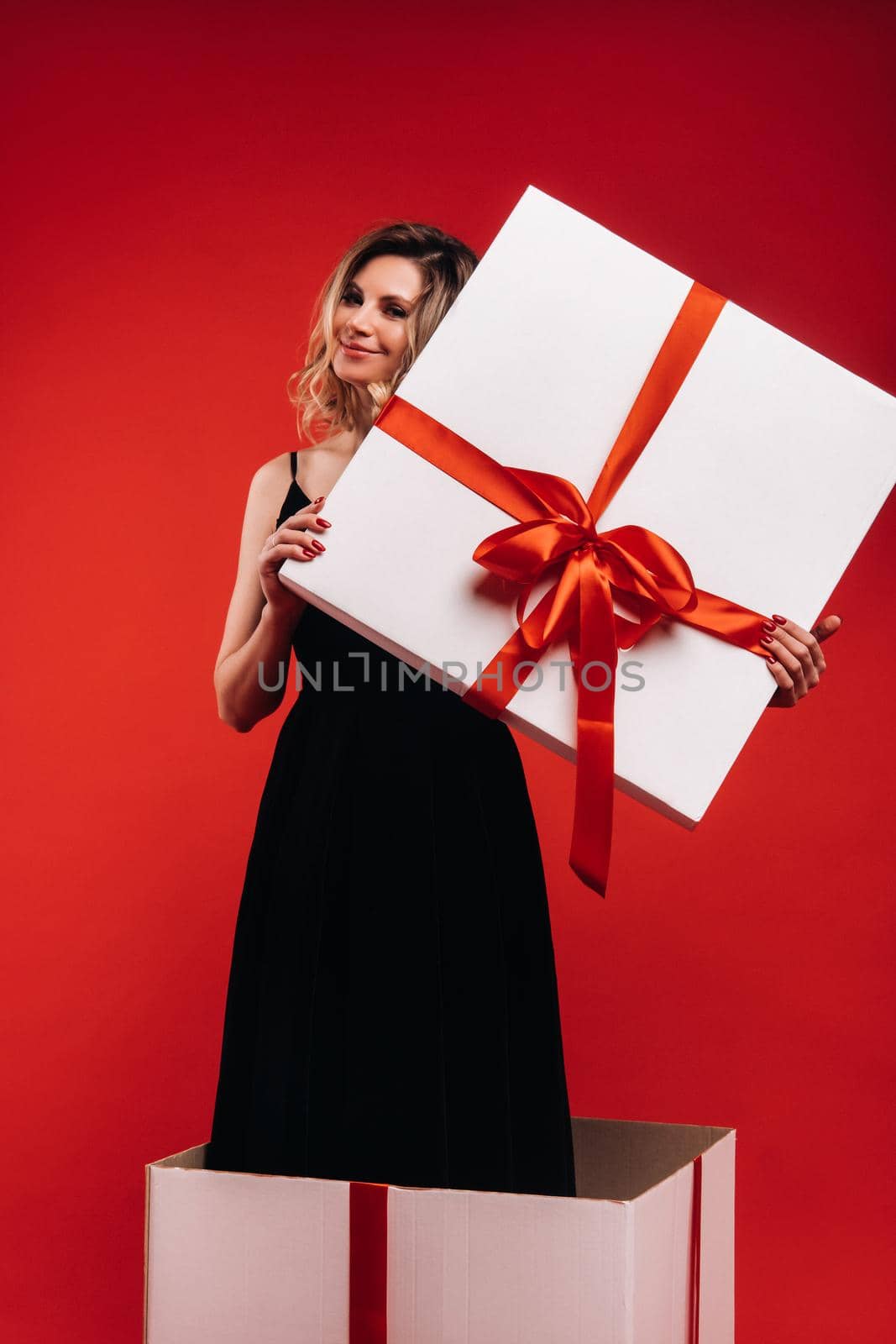a girl in a black dress stands in a gift box on a red background.