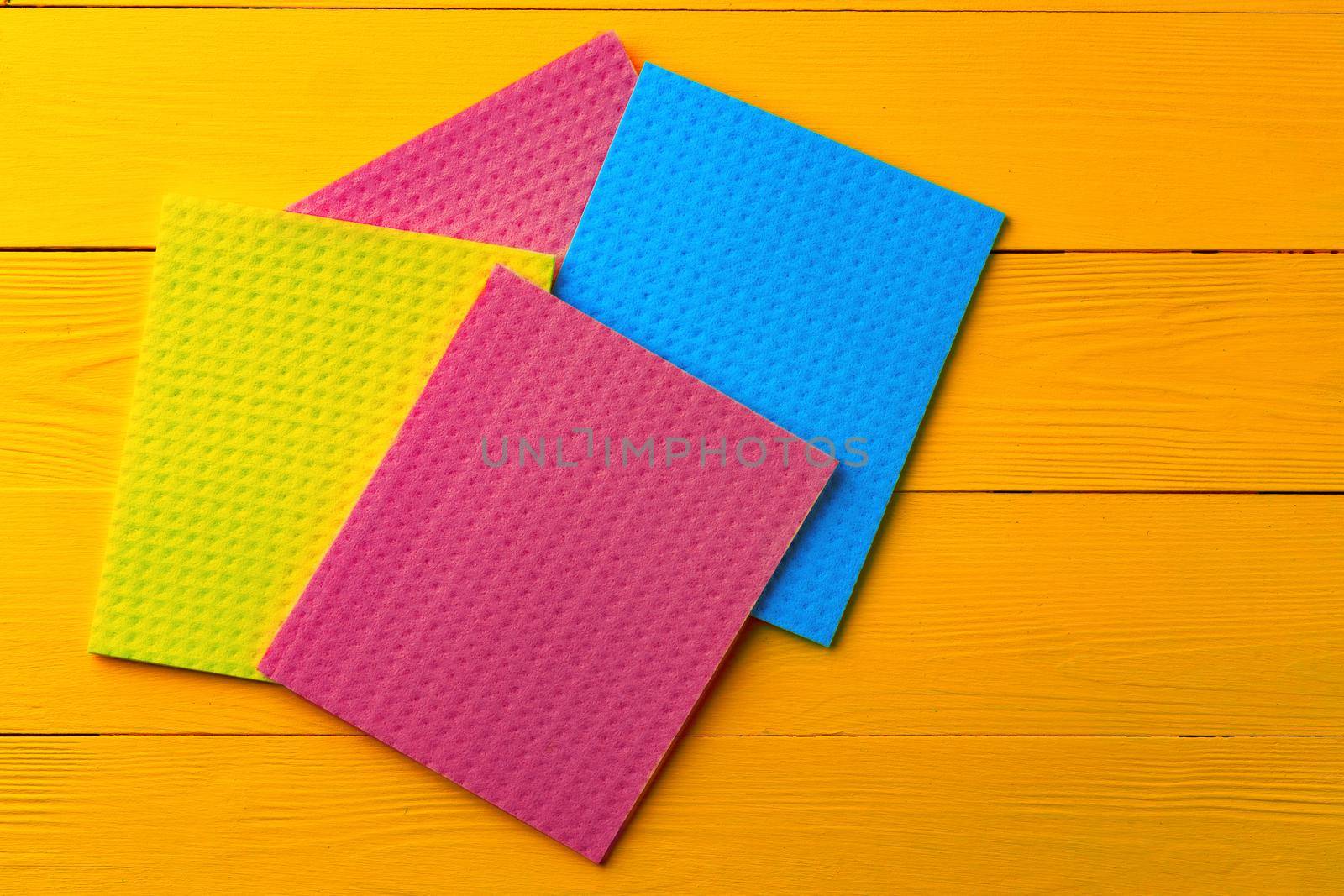 Colored cleaning rags on yellow wooden background, top view
