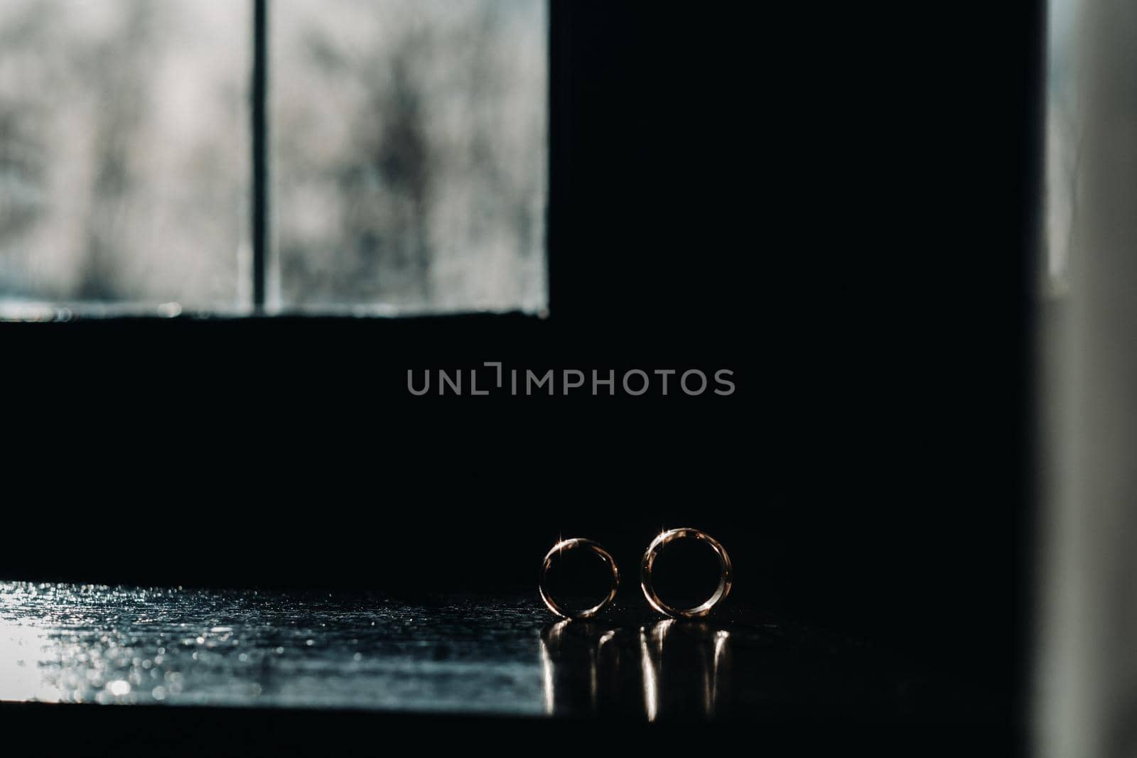 two gold wedding rings on the windowsill in the sunlight by Lobachad