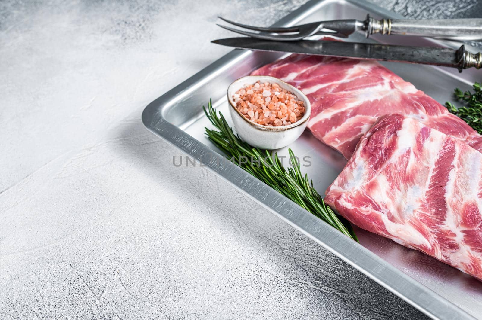 Rack of Raw pork spare ribs in kitchen oven tray with herbs. White background. Top view. Copy space.