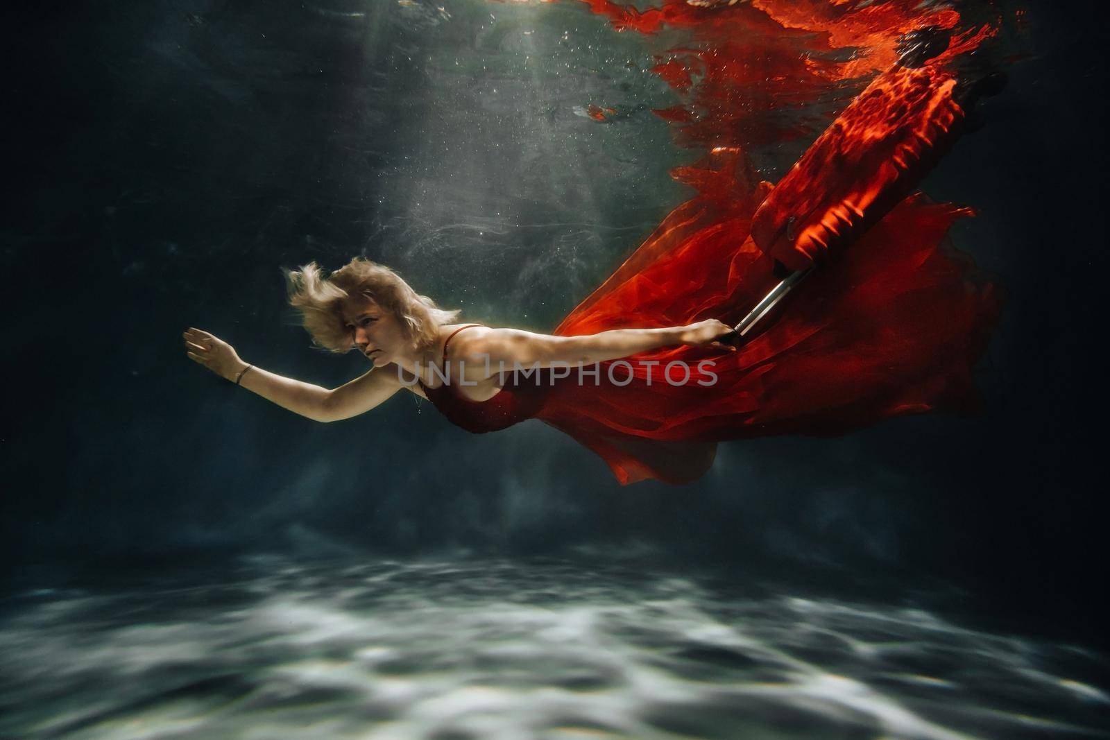 A girl in a red dress is floating under the water with a suitcase.Journey under the water of a single woman.The concept of underwater tourism by Lobachad