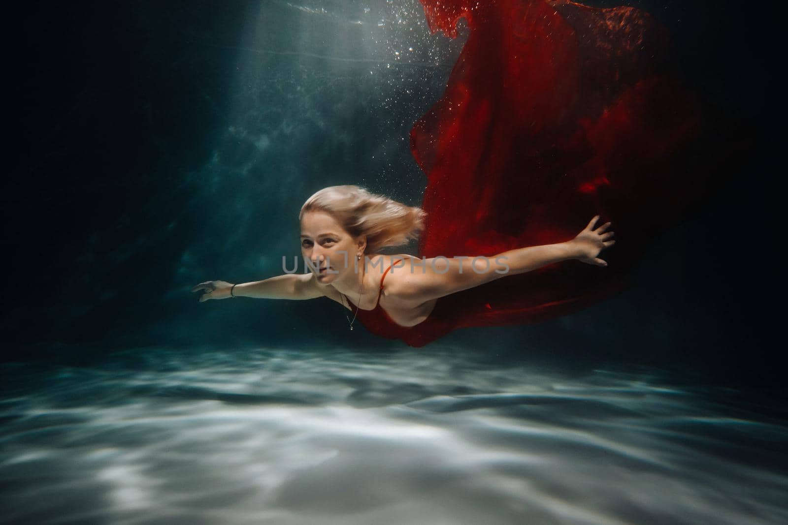 A girl in a red dress is swimming under the water.Journey under the water of a single woman.The concept of underwater tourism by Lobachad