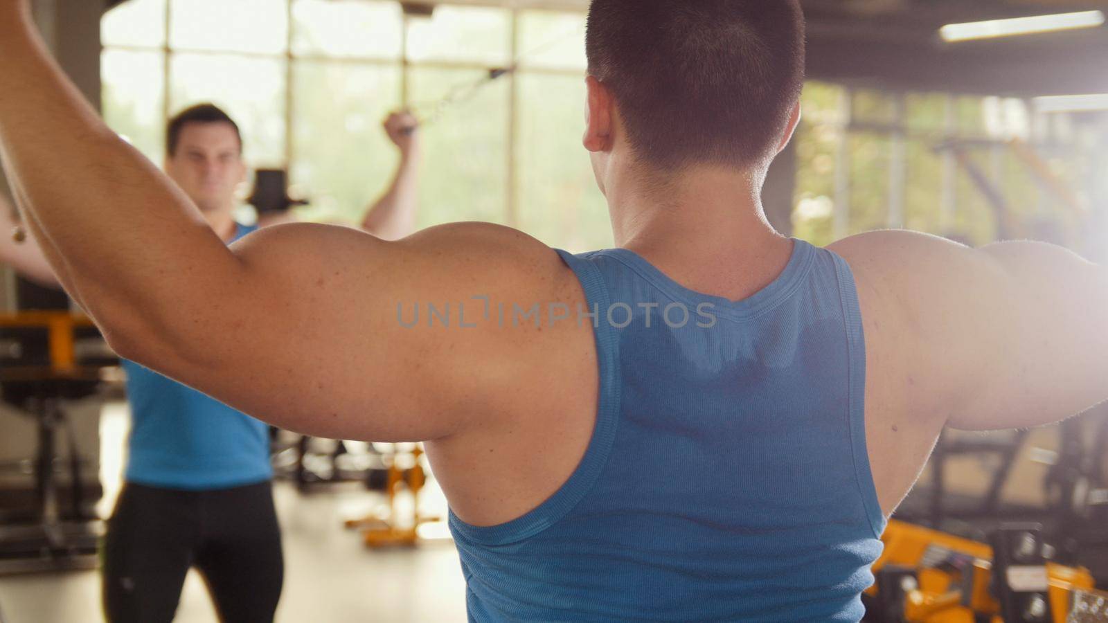 Bodybuilder training in the gym - young muscular man perform training for biceps near mirror, slider