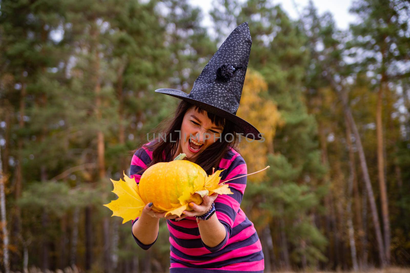 attractive witch with pumpkin in the autumn forest. halloween party concept