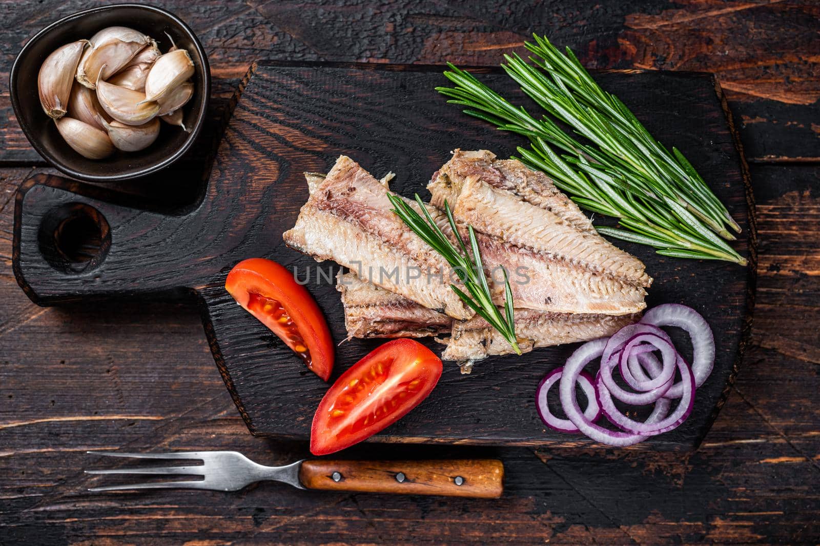 Smoked Sardine fish fillet on wooden board with herbs. Dark wooden background. Top view by Composter