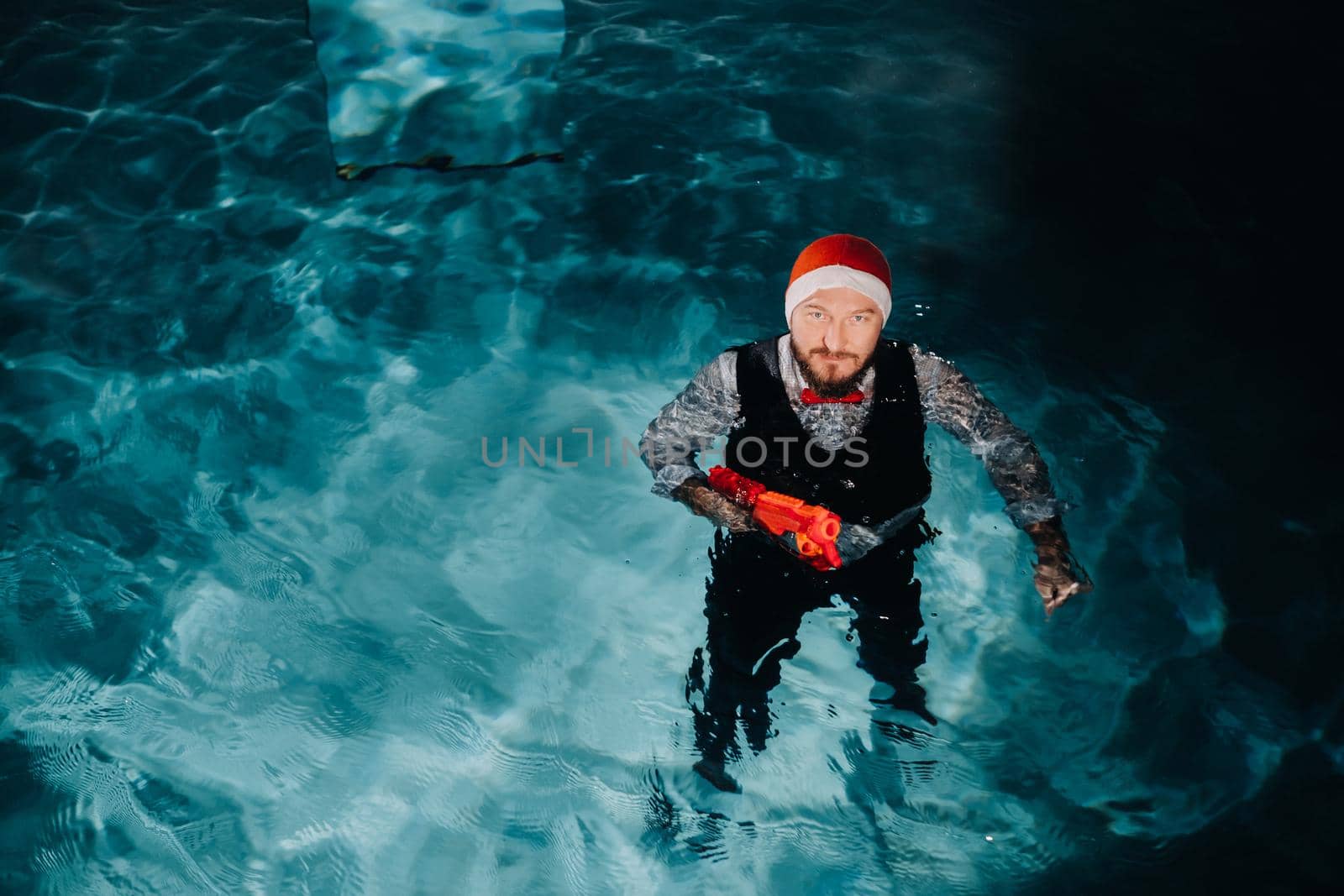 A man in a Santa Claus suit and hat with a red gun in his hands. Santa Claus is swimming underwater with a gun.Christmas concept