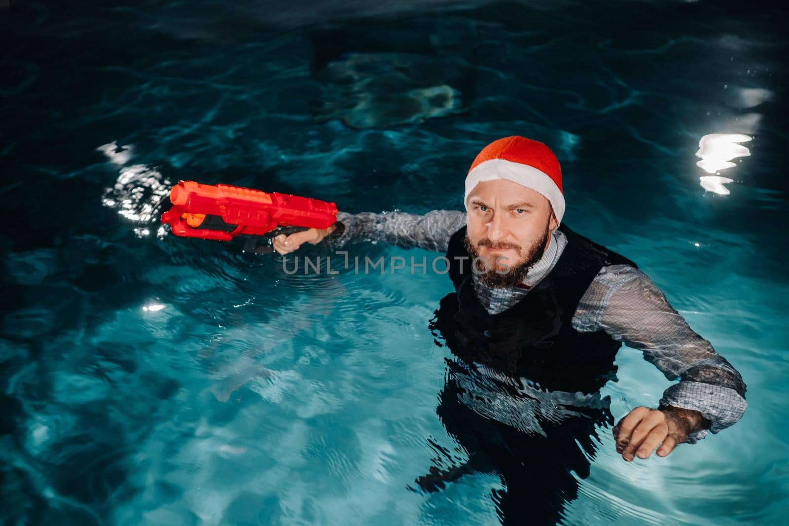 A man in a Santa Claus suit and hat with a red gun in his hands. Santa Claus is swimming underwater with a gun.Christmas concept