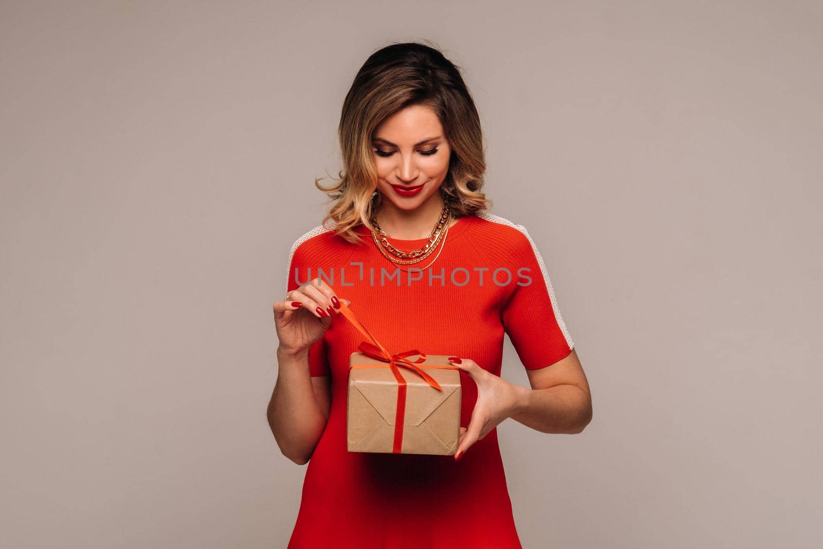 A girl in a red dress stands with gifts in her hands on a gray background.