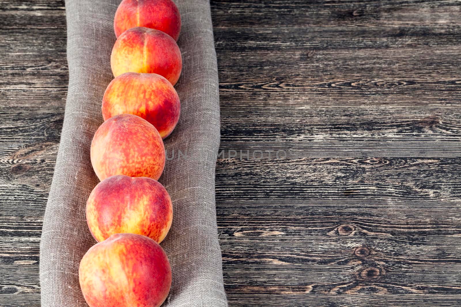 folded in a row on a linen tablecloth ripe orange peaches of a large size, lie on a wooden surface of black color