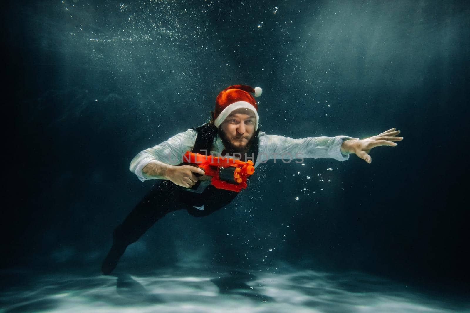 A man under water in a suit and a red gun in his hands. Santa Claus is swimming underwater with a gun.Christmas concept by Lobachad