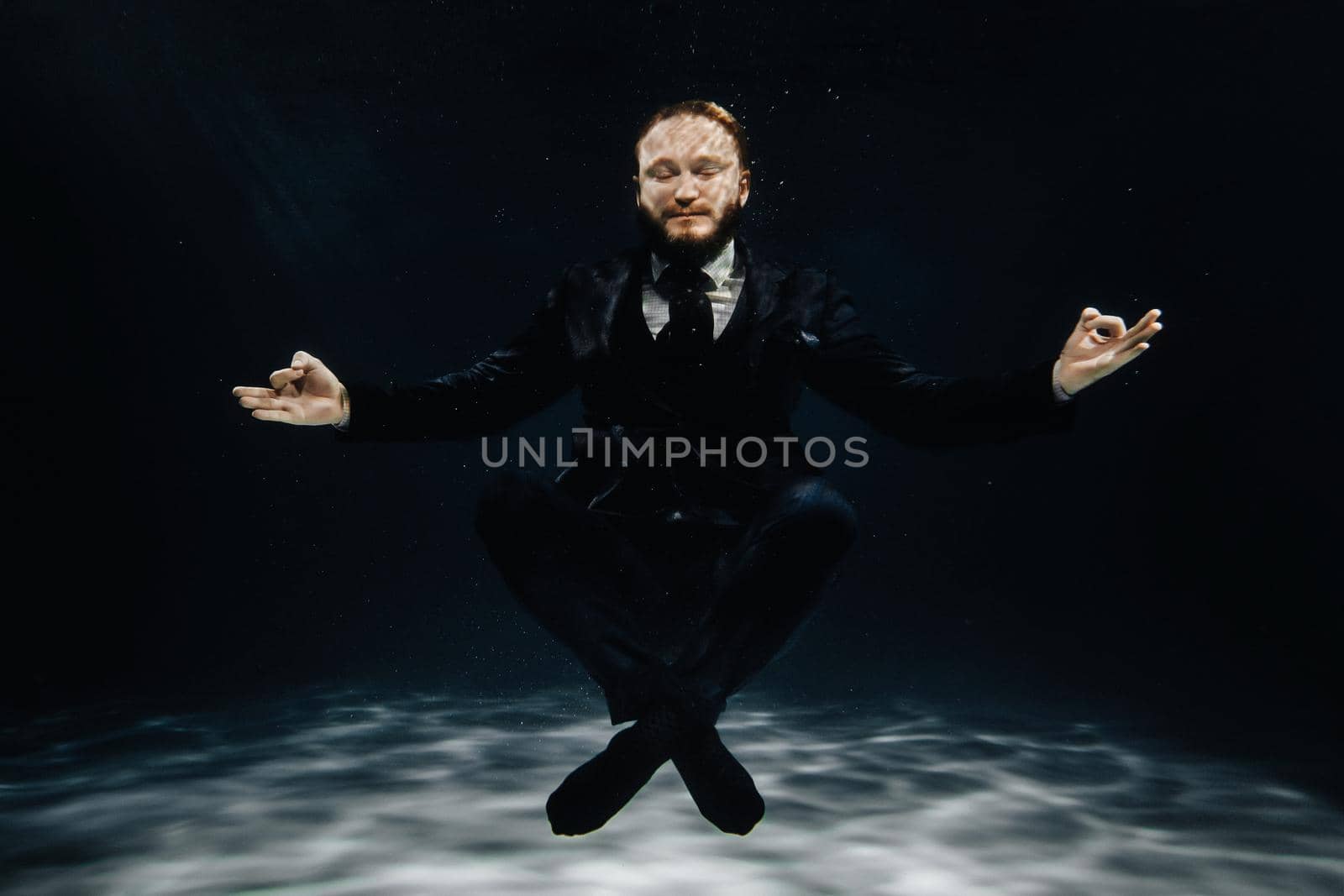 A man in a strict suit under water in the Lotus position.