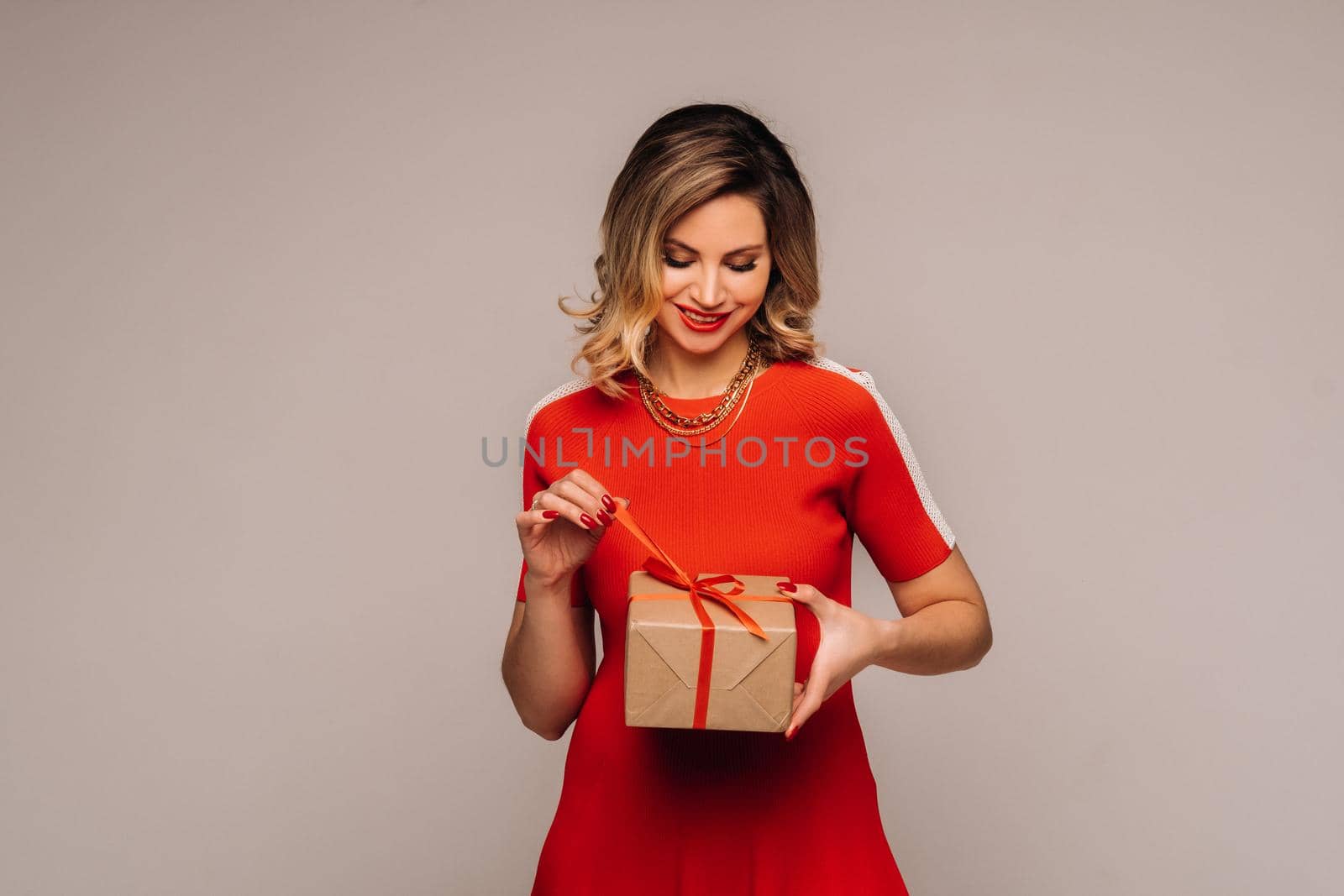 A girl in a red dress stands with gifts in her hands on a gray background by Lobachad