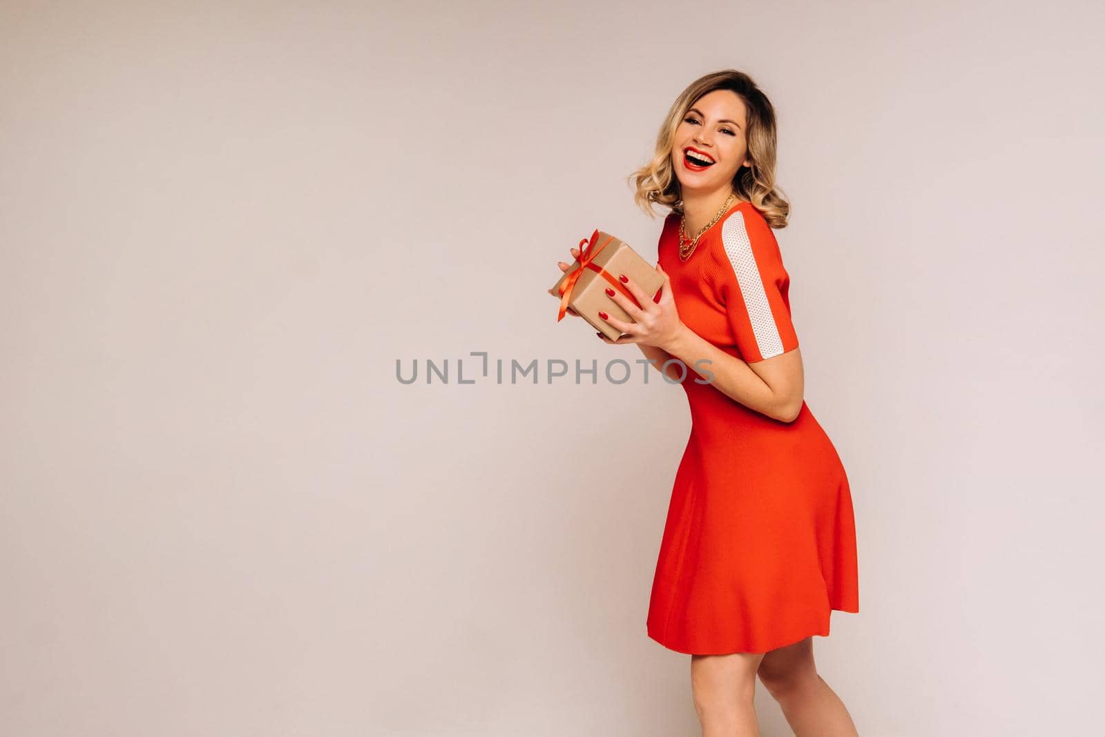 A girl in a red dress stands with gifts in her hands on a gray background by Lobachad
