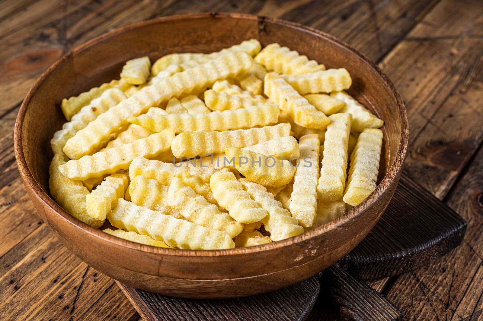 Cold Frozen Crinkle oven French fries potatoes sticks in a wooden plate. Wooden background. Top view by Composter