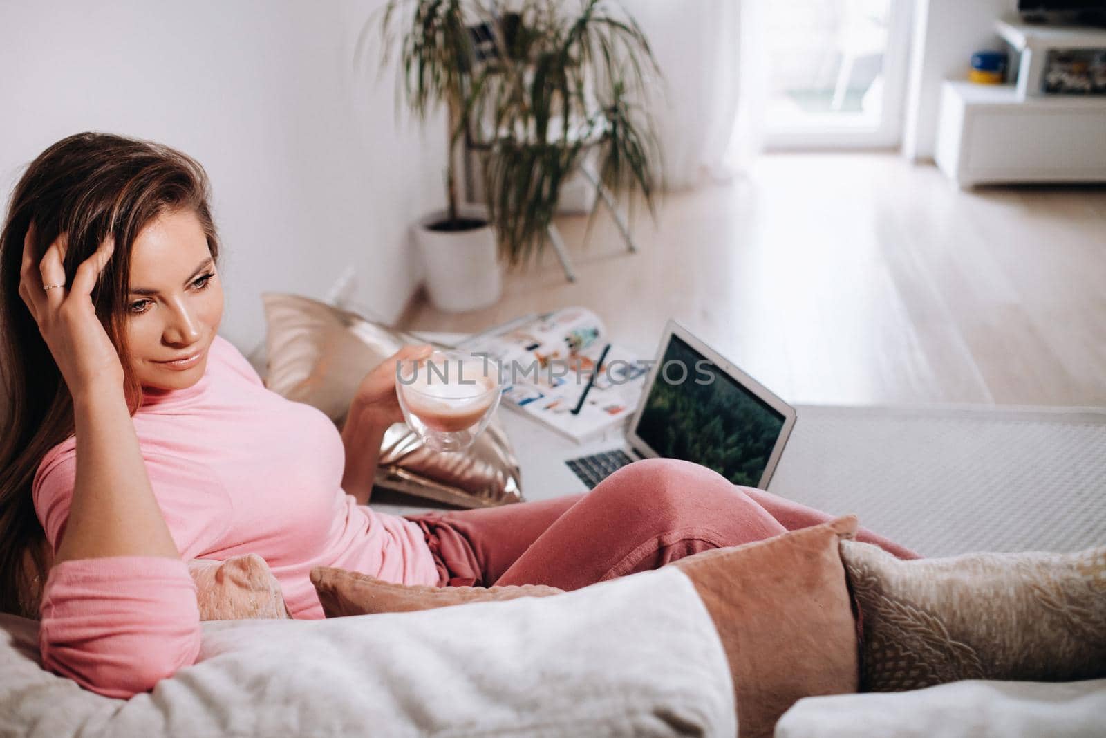 a girl in the morning in pajamas at home working on a laptop with drinking coffee, a girl self-isolated at home and resting on the couch and watching a laptop.Household chores by Lobachad