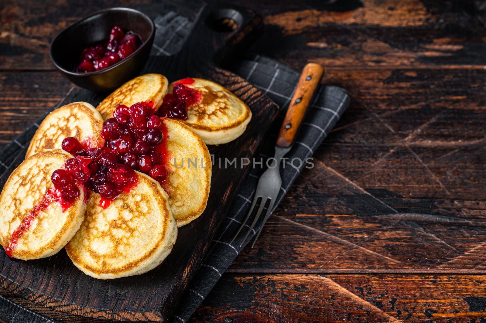 Stack of cranberry syrup pancakes on wooden board. Dark wooden background. Top View. Copy space by Composter