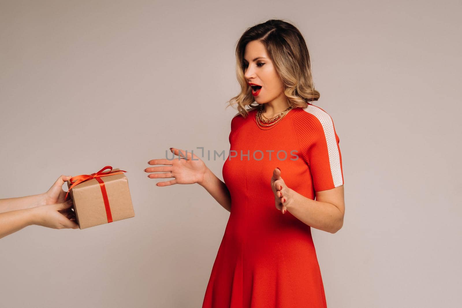 A girl in a red dress is given a gift in her hands on a gray background.