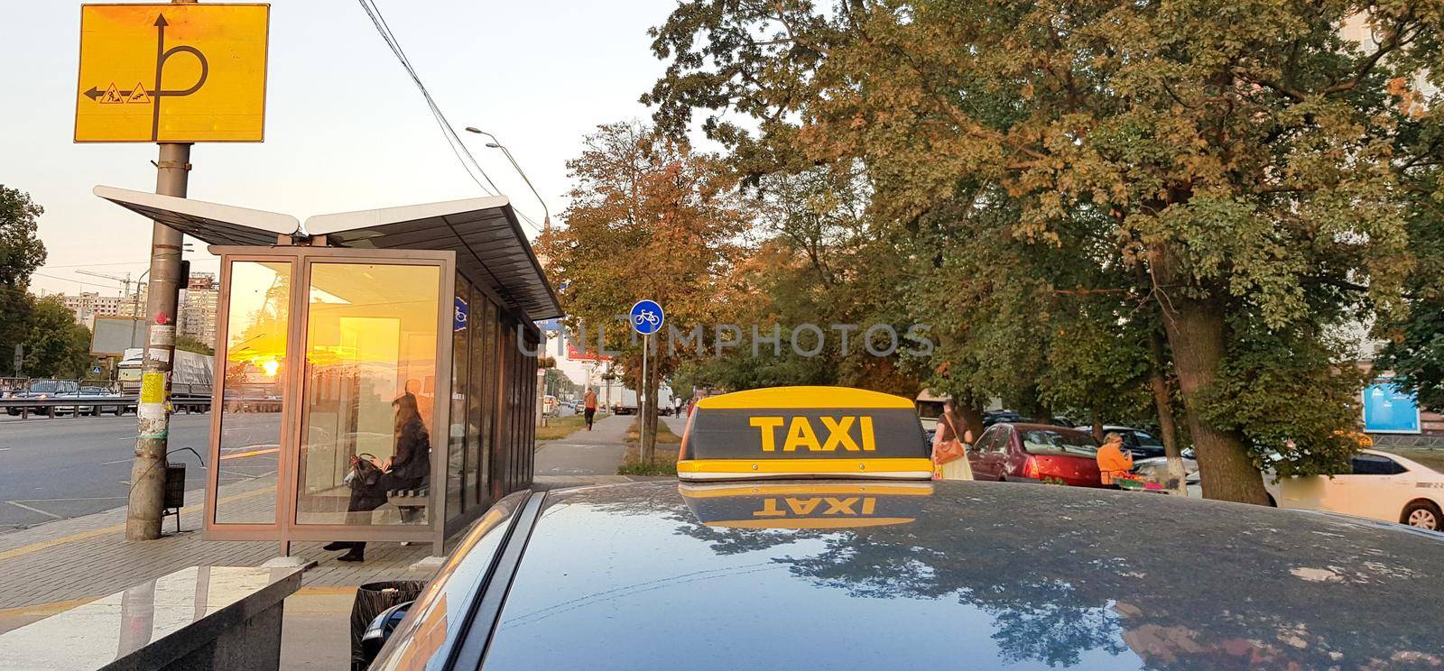 Light box checker taxi bright yellow on the roof of the car on a background of sky, city and people.