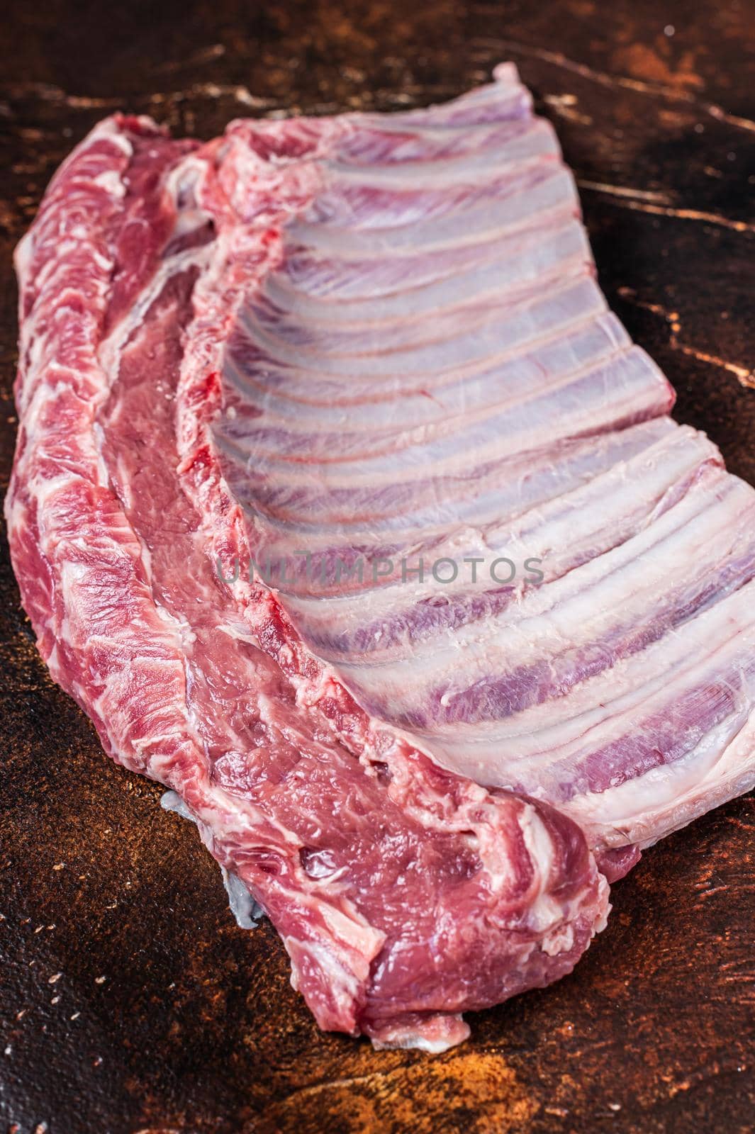 Raw rack of lamb ribs on butcher table. Dark background. Top view.
