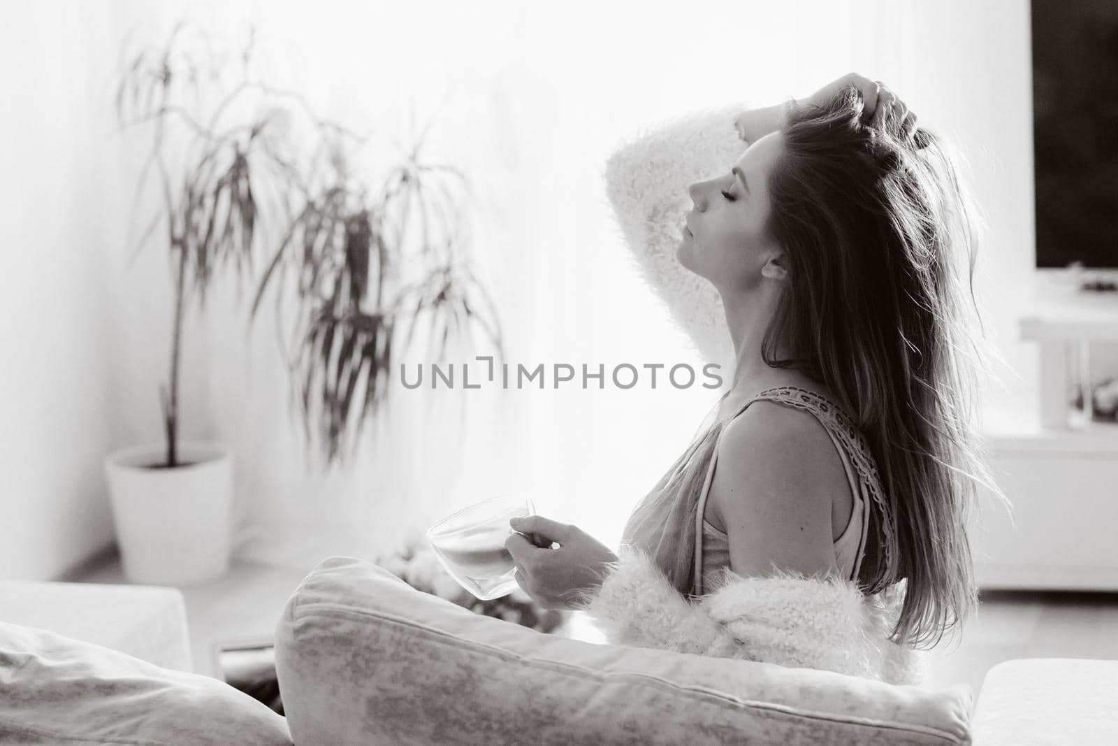 a relaxed girl at home drinks coffee and watches a movie.Domestic calm.The girl is sitting comfortably on the sofa and drinking coffee.black and white photo by Lobachad